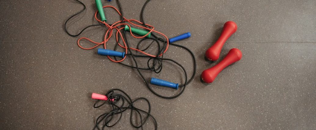 Top view of colorful jump ropes and red dumbbells on a gym floor for fitness activities.