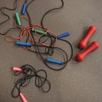 Top view of colorful jump ropes and red dumbbells on a gym floor for fitness activities.
