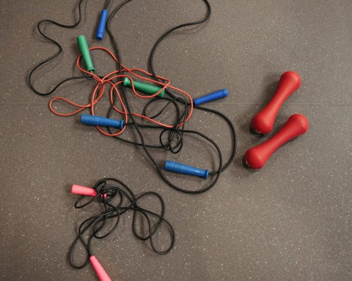 Top view of colorful jump ropes and red dumbbells on a gym floor for fitness activities.